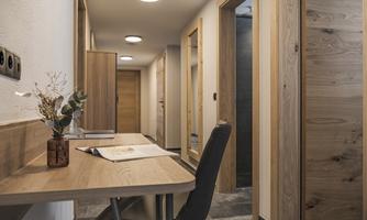 A modern hallway with wooden details and soft lighting. On a table, there is a small plant and documents.