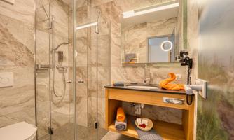 A modern bathroom with a glass shower and elegant marble walls. Towels and personal care items are ready on the sink.
