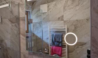A modern bathroom with an elegant sink unit and a large mirror. Towels and a wall shelf are visible in the background.