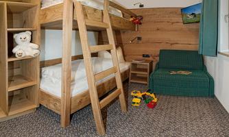 A cheerful children's room with a wooden bunk bed and a comfortable armchair. Toys are scattered on the carpet, and a TV is mounted on the wall.