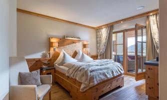 A cozy bedroom with wooden furniture and a large bed. The windows open to a balcony with a view outside.