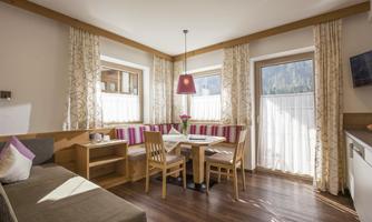 A cozy living area with a dining space and bright curtains. The room has large windows that let in plenty of daylight.