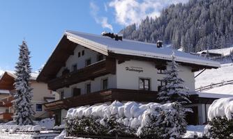 A beautiful snow-covered chalet in the mountains. In the background are wooded slopes and a blue sky.