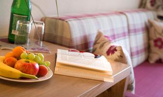 A table with fresh fruit, a book, and a pair of glasses. In the background, a cozy seating area is visible.