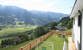 A picturesque view of the mountains and the valley. In the foreground, there is a well-maintained garden with a playground and a soccer goal.