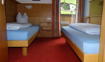 A simple room with two single beds and a red carpet. In the background are windows with a view of a green landscape.