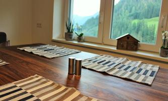 A dining table with striped placemats and two salt and pepper shakers. In the background are windows with a view of green mountains and plants.