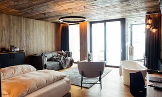 A modern room with a double bed, a cozy couch, and large windows. The wood look creates a warm and inviting atmosphere.