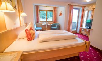 A cozy hotel room with a large bed and a table with chairs. Large windows provide plenty of daylight and a view.