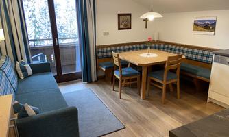 A cozy apartment with a dining area and a couch. Large windows let in plenty of light and offer a view of nature.