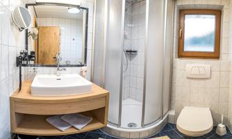 A modern bathroom with a shower cubicle and a sink on a wooden cabinet. The room has bright tiles and a window that lets in natural light.