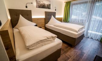 A modern bedroom with two single beds and wood paneling. Large windows ensure plenty of daylight and a cozy atmosphere.