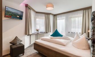 A cozy bedroom with a large bed and modern furniture. Large windows provide plenty of daylight and a pleasant atmosphere.