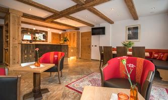 A cozy interior with wooden ceilings and warm light.  
Red armchairs and small tables create an inviting atmosphere.
