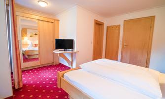 A bright room with two beds and a television. In the background are wooden cabinets and a cozy atmosphere.