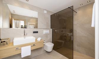 A modern bathroom with bright tiled flooring and elegant sanitary fixtures. The glass shower cabin creates an open and airy space.