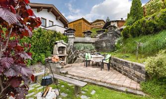 An inviting garden corner with a stone grill and a table for four people. Surrounded by grass and green plants, the area offers a relaxed atmosphere.