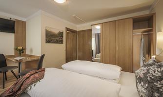 A cozy hotel room with two beds and a table. The decor is modern and in warm wooden tones.
