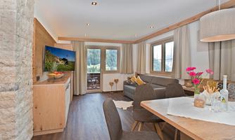 A modern living room with a cozy seating area and a dining table. Large windows provide plenty of daylight and offer a view outside.
