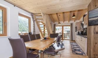 A modern kitchen with a spacious dining table and elegant chairs. Large windows offer a view of the mountain landscape.