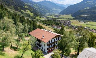 A beautiful house in a picturesque mountain landscape. Lush trees surround the area and the sky is clear and blue.