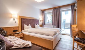 A cozy hotel room with two single beds and a desk.  
Large windows provide plenty of daylight and access to the balcony.