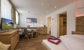 A cozy room with light wooden furniture and a large window. The area is modernly furnished and features a TV as well as a dining area.