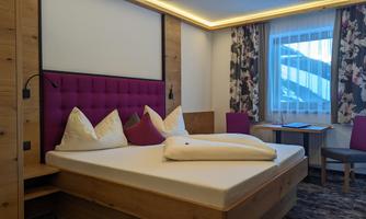 A modern bedroom with a large bed and cozy pillows. The walls are in warm wood tones, and the room has a pleasant, inviting style.
