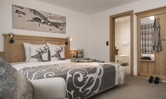 A cozy bedroom with a large bed, decorated with a beautiful blanket and pillows. In the background, doors to a bathroom and another room are visible.