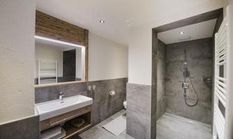 A modern bathroom with a shower and a white sink. The walls are in neutral shades of gray and there is an elegant wooden paneling.