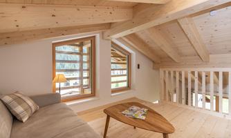 A cozy living space with a wooden ceiling and large windows. A sofa and a table create an inviting atmosphere.