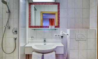 A modern bathroom with a sink, a mirror, and a shower. The walls are tiled with light tiles.