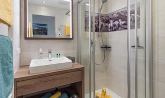 A modern bathroom with a shower and a wooden sink. The walls are light and there are small decorative elements.