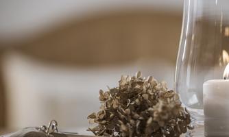 A beautiful decoration with dried flowers, a candle, and a glass carafe. The background is blurred and radiates a cozy atmosphere.