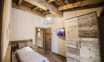 A cozy bedroom with a wooden ceiling and a single bed. A modern wardrobe and a television complete the atmosphere.