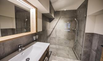 A modern bathroom with a glass shower and an elegant washbasin. The walls are done in neutral shades of gray.