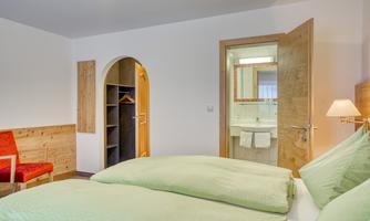 A modern room with two single beds and a cozy seating area. In the background, a bathroom with white fittings is visible.