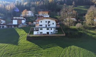 A beautiful house on a green hill overlooking the surrounding landscape. The sun is shining and there are several other houses nearby.