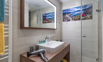 A modern bathroom with an elegant sink and a large mirror. On the wall, there is a colorful picture of a mountain panorama.