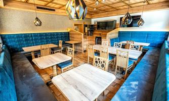 A modern restaurant with wooden decor and comfortable seating. The walls are decorated with blue upholstery and stylish lamps.