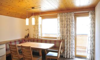 A bright dining room with wooden ceilings and a cozy seating area. Large windows provide plenty of daylight and a view outside.