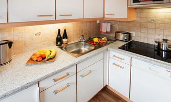A modern kitchen with bright cabinets and a granite countertop. Fresh fruit and two bottles of sparkling wine are on the countertop.