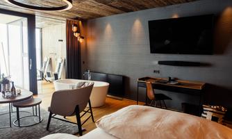 A modern room with a wooden ceiling, a large bed, and a television on the wall. The room features an elegant bathroom and cozy furniture.
