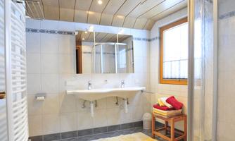 A modern bathroom with a double sink and large mirrors. The shower is in a separate corner, and there are bright towels as well as a chair.