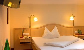 A cozy hotel room with a double bed and a bright ceiling. There is a table with a magazine and fresh fruit, as well as a television on the wall.