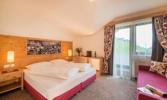 A modern hotel room with a cozy double bed and a red seating area. Large windows provide plenty of daylight and a beautiful view.
