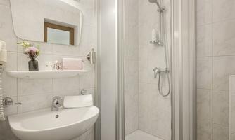 A modern bathroom with a shower and a small sink. The walls are bright and tile-like, with decorative elements such as a floral vase.