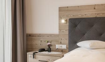 A cozy bedroom with a modern bed and a wooden nightstand. On the nightstand, there is a small flower vase and a telephone.