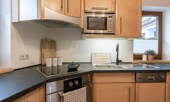 A modern kitchen with wooden cabinets and dark countertops. There is a stove, a sink, and some decorative elements by the window.