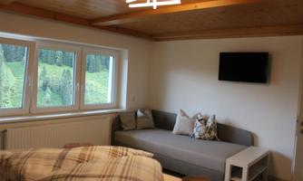 A cozy living space with a gray sofa and a small table. Large windows provide a view of the green landscape outside.